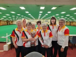 Image of eight Kingsthorpe Bowling Club ladies in club colours celebrating their win in the 2023 Ivy & Horrace Tarrant Trophy at Northampton & District Bowling Club